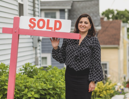 Smiling Female Real Estate Agent Standing Next to a Sold Sign